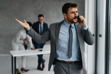 Naklejka premium Angry businessman shouting on the phone in a busy office, representing a business crisis or high-stress situation