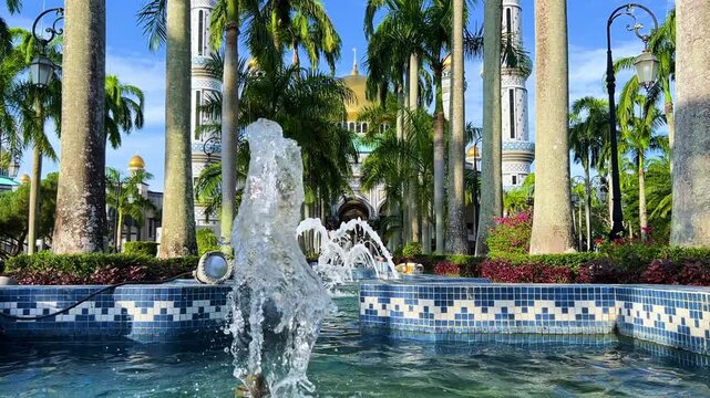 The golden dome and building of the Jamil Asra Hassan Al-Bolkiah Mosque in Bandar Seri Bagawan, Brunei Darussalam, are framed by tropical palm trees on a sunny day. Asia. 4К