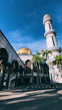 The golden dome and building of the Jamil Asra Hassan Al-Bolkiah Mosque in Bandar Seri Bagawan, Brunei Darussalam, are framed by tropical palm trees on a sunny day. Asia. 4К