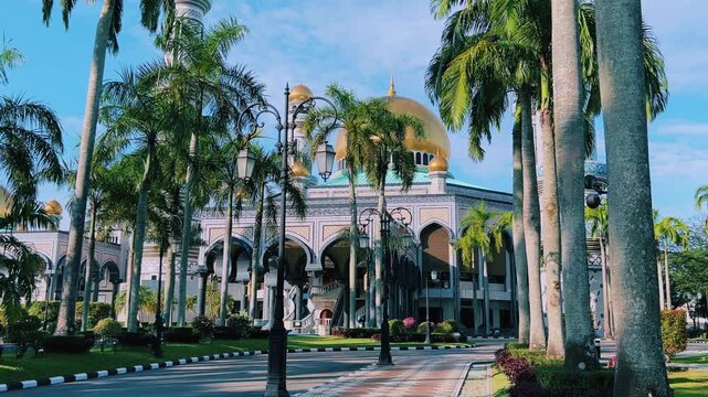 The golden dome and building of the Jamil Asra Hassan Al-Bolkiah Mosque in Bandar Seri Bagawan, Brunei Darussalam, are framed by tropical palm trees on a sunny day. Asia. 4К
