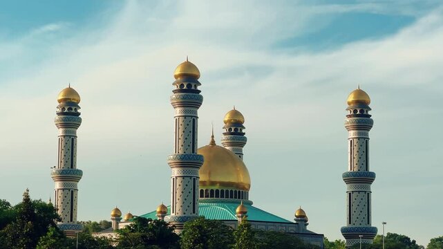 The golden dome and building of the Jamil Asra Hassan Al-Bolkiah Mosque in Bandar Seri Bagawan, Brunei Darussalam, are framed by tropical palm trees on a sunny day. Asia. 4К