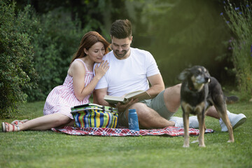 Happy couple sitting in nature and reading a bookmwith their dog