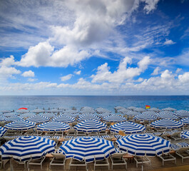 Pebble beach along Promenade des Anglais with beach umbrellas and chairs with the turquoise water of the Mediterranean Sea in Nice, Cote d'Azur France