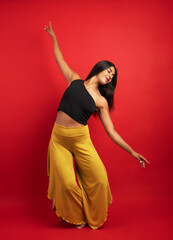 Young latina woman performing fluid dance movements with passion on a red background