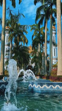 The golden dome and building of the Jamil Asra Hassan Al-Bolkiah Mosque in Bandar Seri Bagawan, Brunei Darussalam, are framed by tropical palm trees on a sunny day. Asia. 4К
