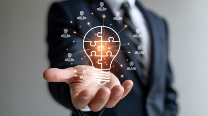 Business innovation and teamwork concept with lightbulb puzzle and people icons floating above businessman hand, creative collaboration