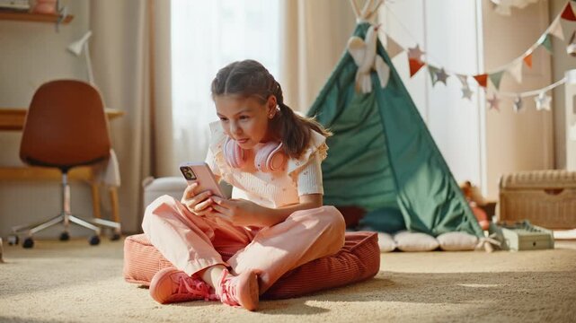 Involved kid playing smartphone browsing internet relaxing at cozy room carpet