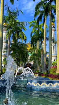 The golden dome and building of the Jamil Asra Hassan Al-Bolkiah Mosque in Bandar Seri Bagawan, Brunei Darussalam, are framed by tropical palm trees on a sunny day. Asia. 4К