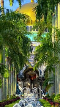 The golden dome and building of the Jamil Asra Hassan Al-Bolkiah Mosque in Bandar Seri Bagawan, Brunei Darussalam, are framed by tropical palm trees on a sunny day. Asia. 4К