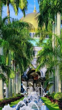 The golden dome and building of the Jamil Asra Hassan Al-Bolkiah Mosque in Bandar Seri Bagawan, Brunei Darussalam, are framed by tropical palm trees on a sunny day. Asia. 4К