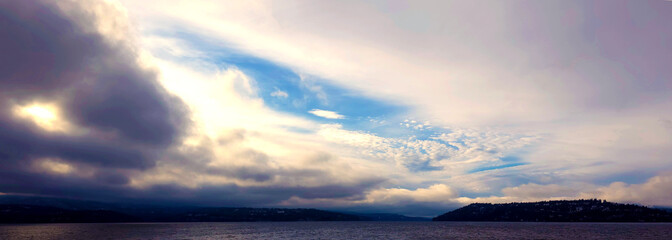 Long Panoramic Photo of Sunset Billowy and Sweeping Clouds in Sky Over a Lake with Contrast of Lights and Darks