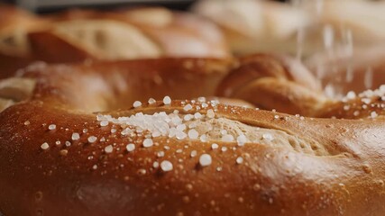A closeup shot captures the moment coarse sea salt crystals are generously sprinkled onto the goldenbrown freshly baked surface of a delicious pretzel highlighting the texture and appetizing appeal o.
