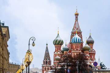 Fototapeta premium Moscow, Russia, A view of St. Basil's Cathedral and the Spasskaya Tower of the Kremlin in Moscow, Russia, during winter. Snow-covered domes and festive street lamps in the foreground.