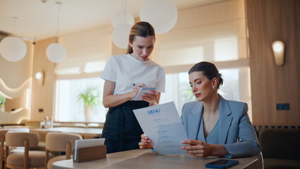 Obraz premium Restaurant guest talking waitress reading menu making order at cozy cafe closeup