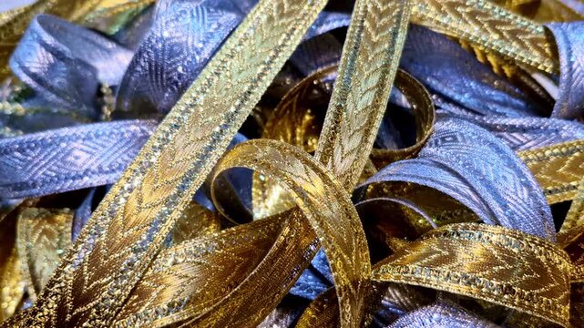 A close-up of metallic gold and silver decorative lace ribbons intertwined together, showing embossed patterns and reflective textures commonly used for gift wrapping or festive decoration.
