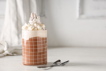 Glass of hot cocoa drink with whipped cream and marshmallows on white wooden table