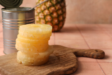 Wooden board and tin can with canned pineapple rings on beige tile table
