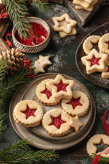 Homemade Linzer Christmas cookies filled with raspberry jam and dusted with sugar on ceramic plate with fir tree branches and festive decorations