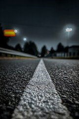 Low angle view of deserted road at night with white line and blurred city lights in distance