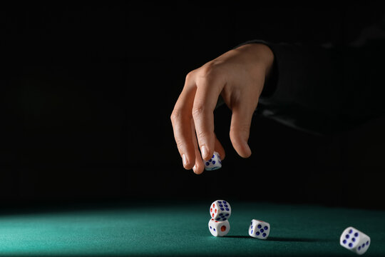 Male hand throwing white game dices on green table against black background