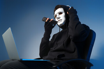 Male fraudster in headphones with laptop talking by mobile phone on light background