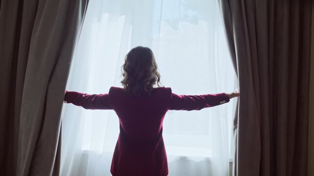 Back woman moving curtains letting morning sunlight in modern apartment closeup.
