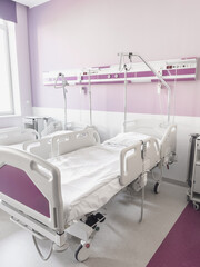 Vertical photo showing a modern and sterile hospital room with two empty medical beds in a bright interior with purple walls in natural daylight