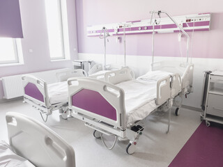 A bright, horizontal shot of a modern and sterile sick room with three empty medical beds against the background of purple walls, illuminated by natural daylight in clinical conditions, depicting the 