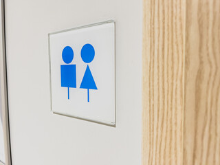 Minimalist blue sign of women's and men's toilet on a clean white wall next to a wooden door frame, bright interior lighting, horizontal orientation photos