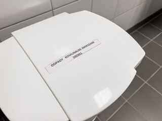 Modern white plastic waste bin mixed with Polish label on gray tiles in bright sterile interior horizontal orientation photos "Odpady Komunalne Zmieszane"