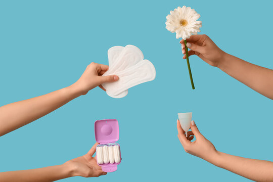 Female hands with menstrual cup, pads and tampons storage box on blue background