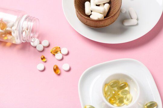 Plates, wooden bowl and bottle with different pills on pink background
