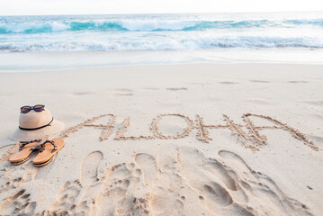 Aloha word written in sand with hat and flip-flops © Sulbha