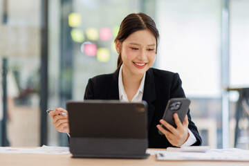 Fototapeta premium Asian businesswoman holding phone work on laptop computer at the office with calculator document doing planning analyzing the financial report, business plan investment, finance analysis concept. 
