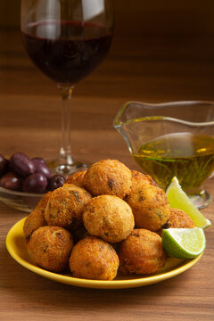 Cod fritters, a glass of red wine, black olives, and olive oil