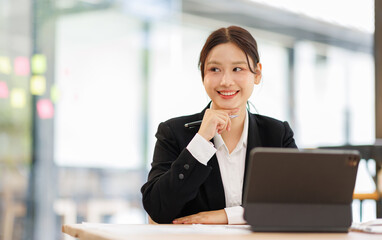 Fototapeta premium Portrait of a confident and smiling Asian business woman working on tablet at her desk in a modern office. 