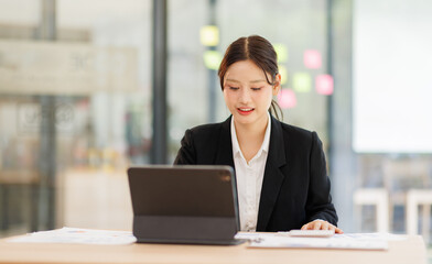 Fototapeta premium Portrait of a confident and smiling Asian business woman working on tablet at her desk in a modern office. 