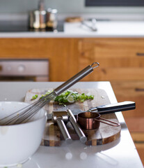 Mesada preparada para cocinar con un bolw, batidor, tabla, chuchillo, pica ajo, medidor de bronce