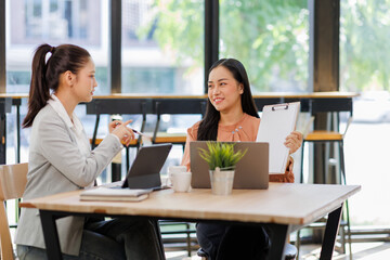 Fototapeta premium Smiling two asian accountant women working with documents using calculator and laptop computer at office desk 
