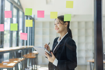 Business asian woman use post it notes to share idea sticky note on glass wall,  planning and...