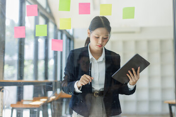 Business asian woman use post it notes to share idea sticky note on glass wall, planning and Brainstorming thinking sticky History notes concept.