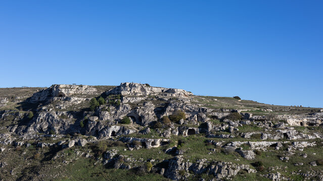 ancient paleolithic cave dwellings carved into the rocky cliffs of murgia materana park under a clear blue sky in basilicata, southern italy