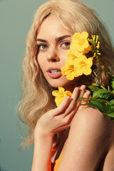 A young woman with long blonde hair surrounded by vibrant yellow flowers, showcasing natural beauty and joyful emotions against a soft green background.