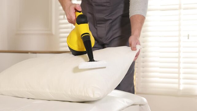 Pest control worker cleaning pillow with steam cleaner indoors, closeup