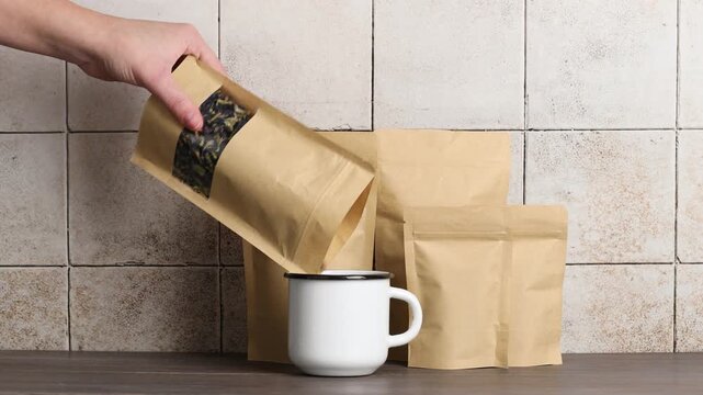 Woman pouring flower tea into cup from stand-up pouch at wooden table, closeup
