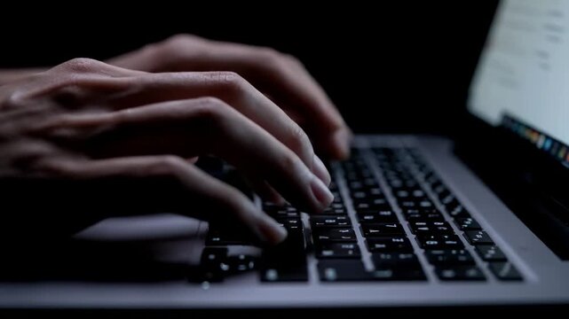 Close-up of hands typing on a backlit laptop keyboard at night, focused fingertips in low light glow