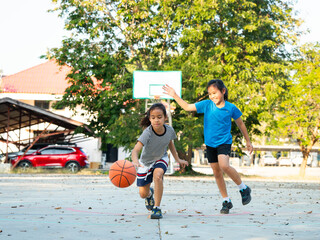 Two young girls playing basketball together on outdoor court