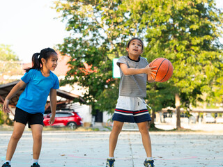Two young girls playing basketball together on outdoor court