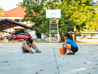 Two young girls resting with basketball on outdoor court