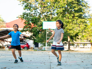 Two young girls playing basketball together on outdoor court